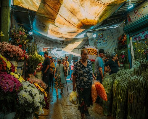 A person walking through a vibrant, moderately busy Mexican city market during the day